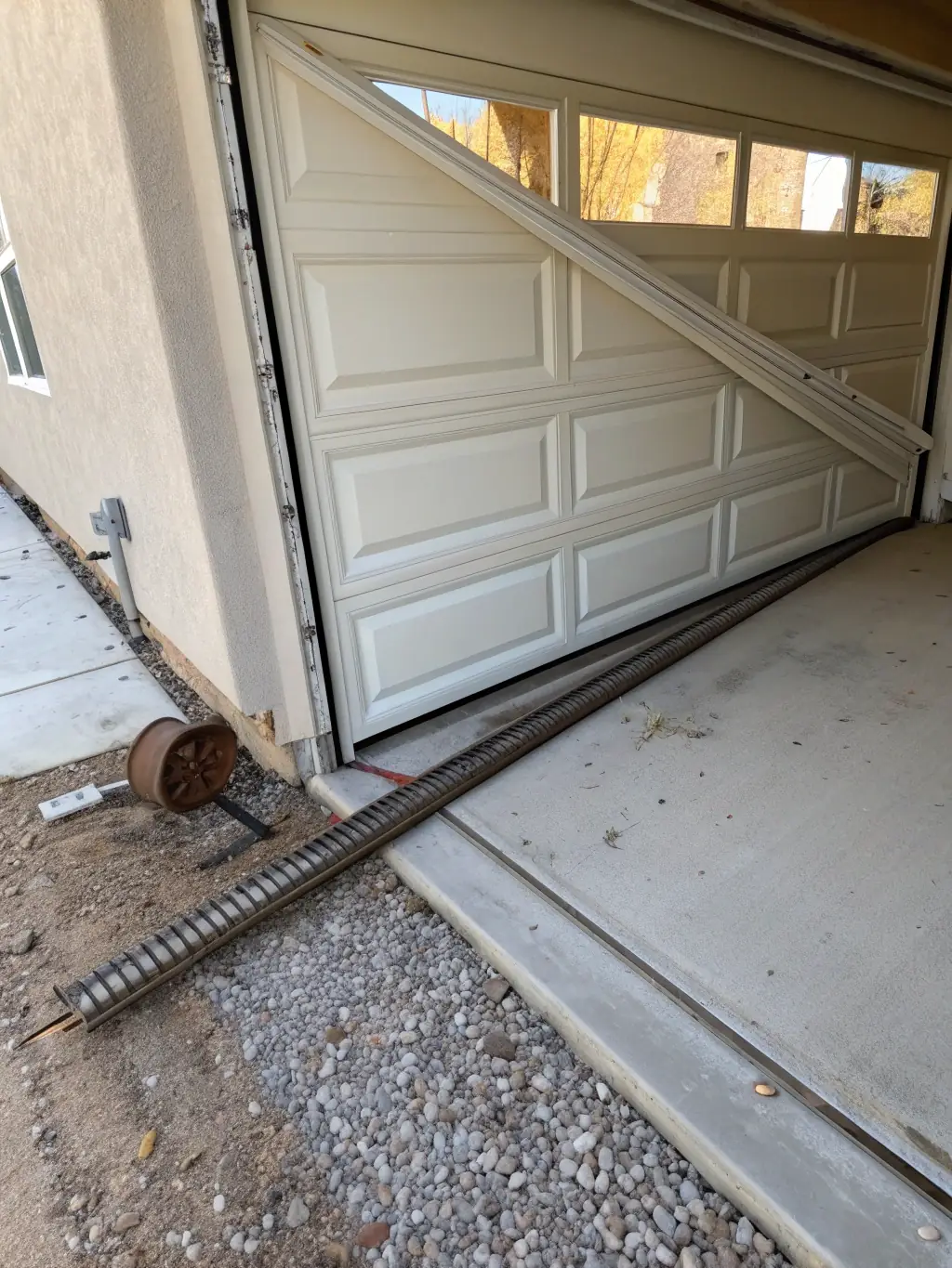 An image of a garage door hanging unevenly, with a visible gap on one side, indicating that the door is off track. The setting should be a typical suburban home.